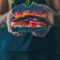 person holding meat sandwich with sliced tomatoes, onions, and grilled meat